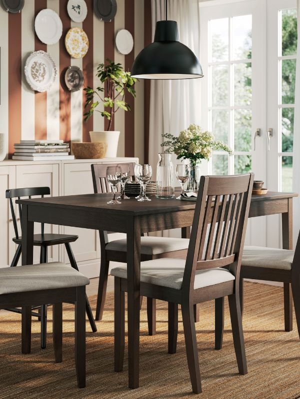 Cozy dining room with SKURUP lamp, NÄSINGE table, LOHALS rug, SVALKA glasses, VARDAGEN jug, GLADELIG tableware and SOJABÖNA pot.
