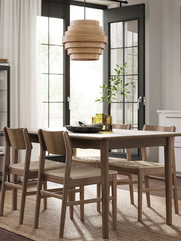 Natural dining area with DYKARKLOCKA shade, SKANSNÄS table, LOHALS rug, LILL curtains and KONSTFULL vase.