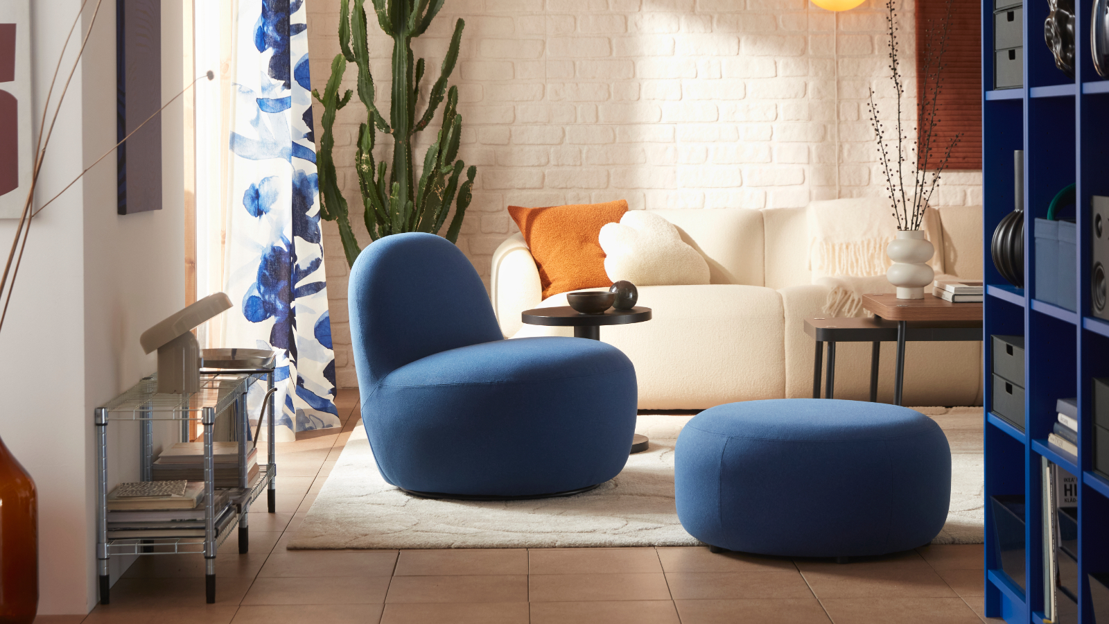 A living room with a Gunnared dark blue LILLESÄTER swivel easy chair in soft fabric beside an off-white sofa and green plants.