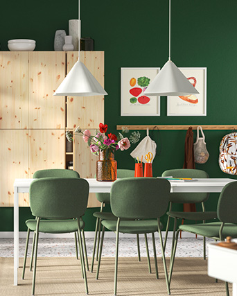 Comedor con pared verde, sillas a juego, mesa blanca, lámparas cónicas y un aparador de madera clara.