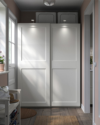 Armario blanco con puertas lisas en un pasillo luminoso con luz natural.