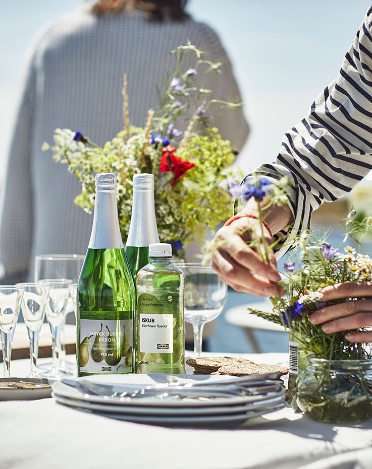  Table set with bottles of sparkling pear drink and elderflower water, alongside shared plates of food during an outdoor gathering by the water