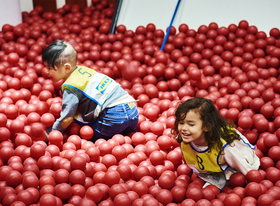 Two children playing and laughing in a red ball pit in a kids’ play area.