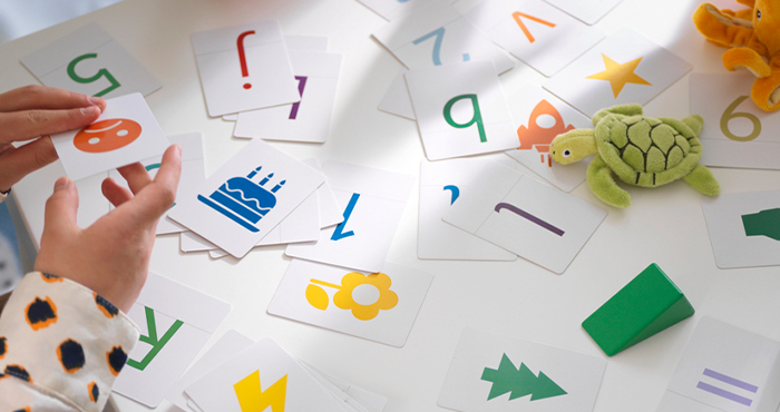 A child’s hands playing with educational cards featuring letters, numbers, and illustrations on a table.