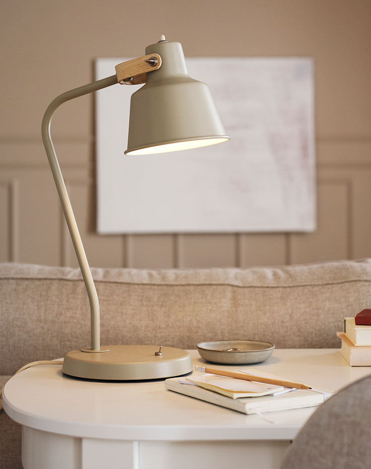 A beige/ash SJÖMAKT desk lamp stands on top of a white ROSENTORP desk along with a pencil and a notebook.