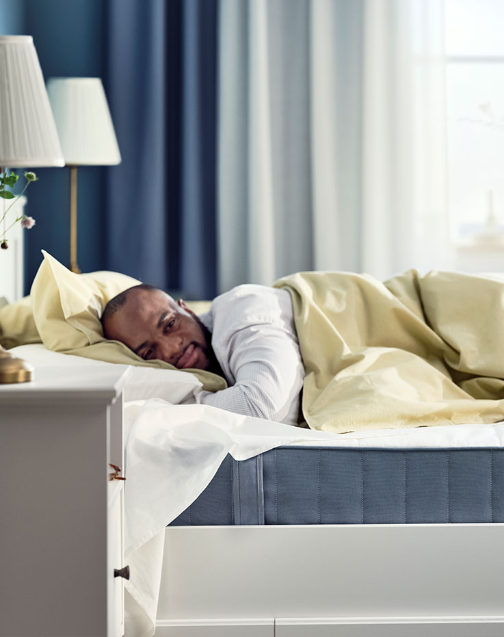 A person comfortably sleeping on a modern style bed, the blue mattress is visible, in the background 