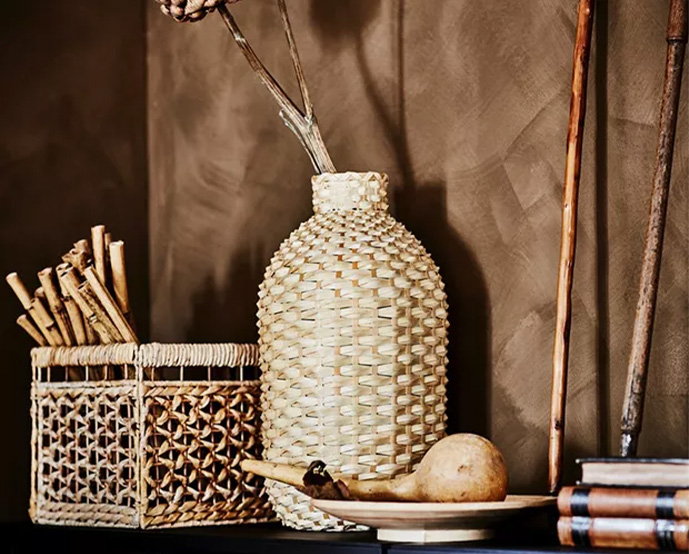 Decorative natural fiber vase next to woven baskets and books in a warm rustic-style setting.