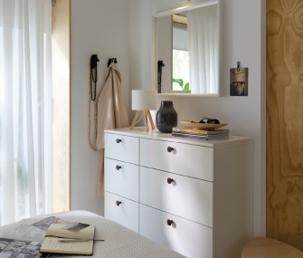 Dormitorio luminoso con cómoda blanca, espejo y decoración