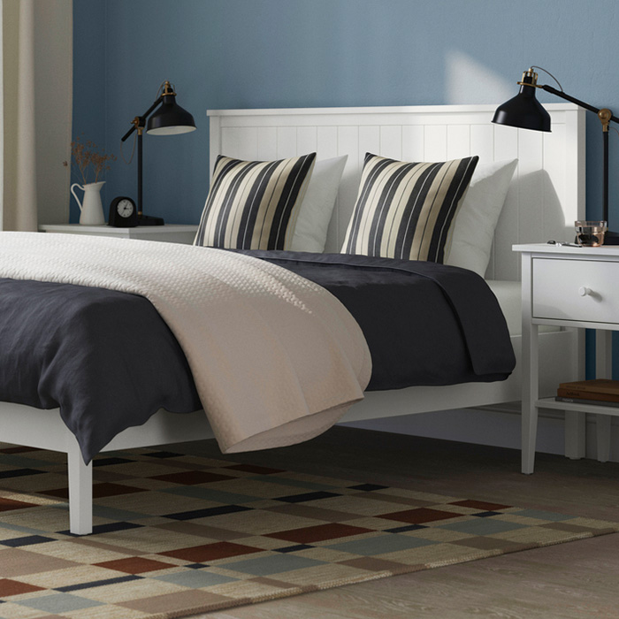 Un dormitorio moderno con cama blanca, cojines de rayas, lámparas negras y una alfombra geométrica multicolor.