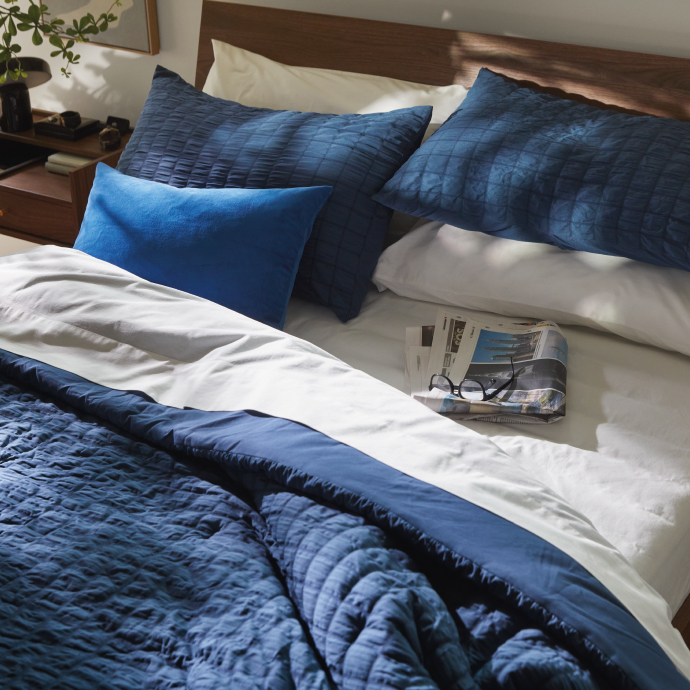 Cama ordenada con ropa de cama azul y una revista.