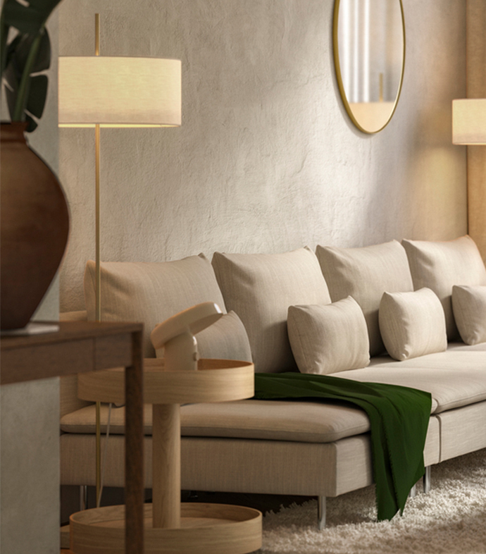 Un ambiente de sala de estar minimalista con un gran sofá beige, una manta verde, una mesa auxiliar de madera clara, una lámpara de pie y un espejo redondo con borde dorado sobre una pared texturizada.