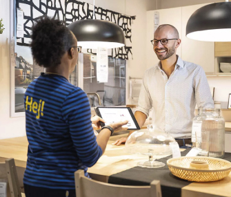 IKEA employee showing a tablet to a smiling customer in a kitchen showroom.