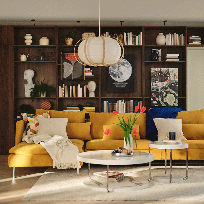Cozy living room with a large yellow sectional sofa, two white coffee tables with red tulips, and a wall-to-wall dark wood bookcase.