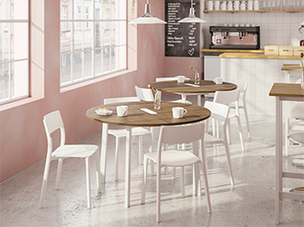 Cafetería luminosa con mesas redondas de madera, sillas blancas y paredes de tono rosado.
