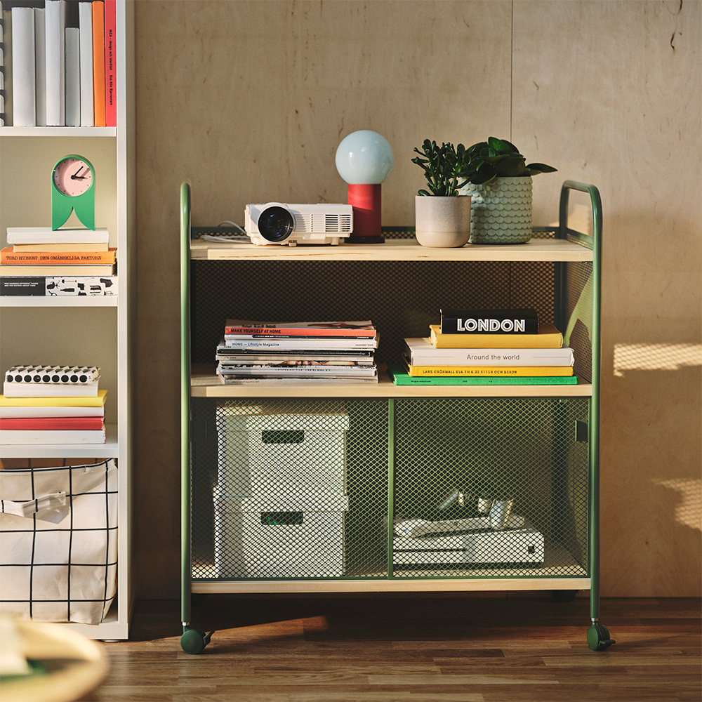 A living room with a dark green NALMAKARE cabinet on castors, displaying books and a plant on a shelf.