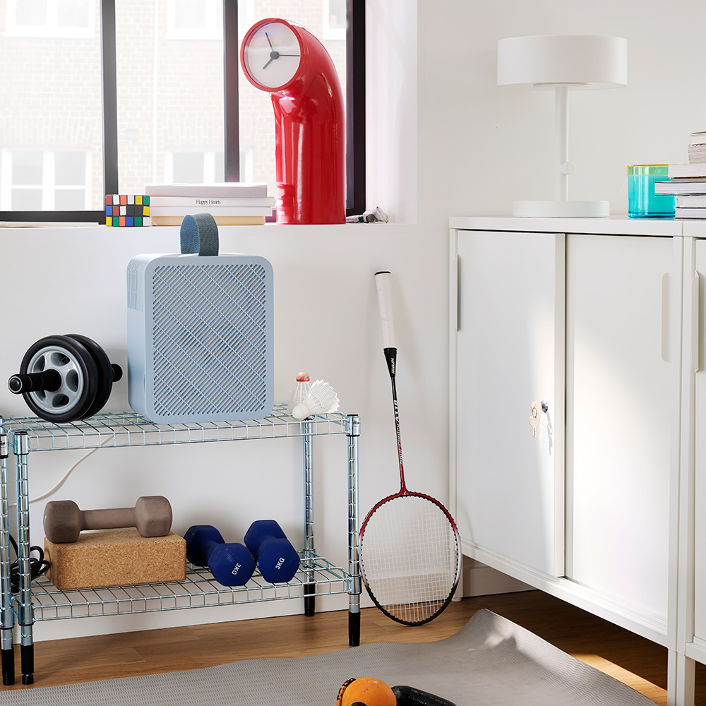 A gym corner features a blue UPPATVIND air purifier on a shelf, next to weights and a yoga mat on the floor.