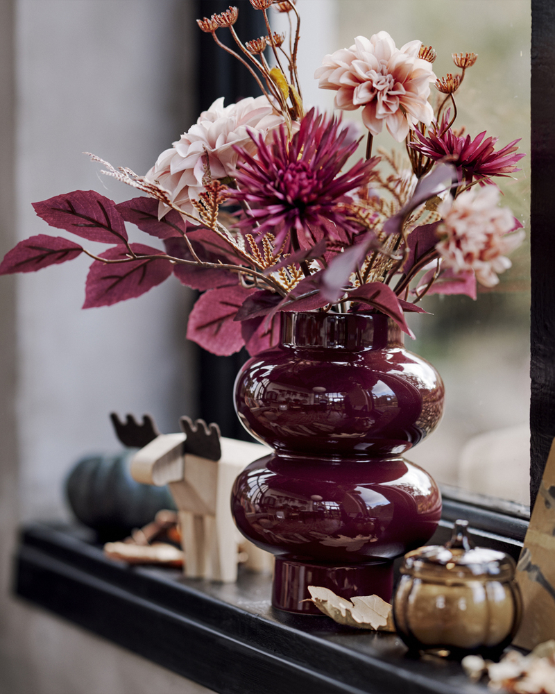 A pink SMYCKA artificial bouquet is in a brown-red PÄRLHÄGG vase, along with HÖSTAGILLE decorative items on a windowsill.