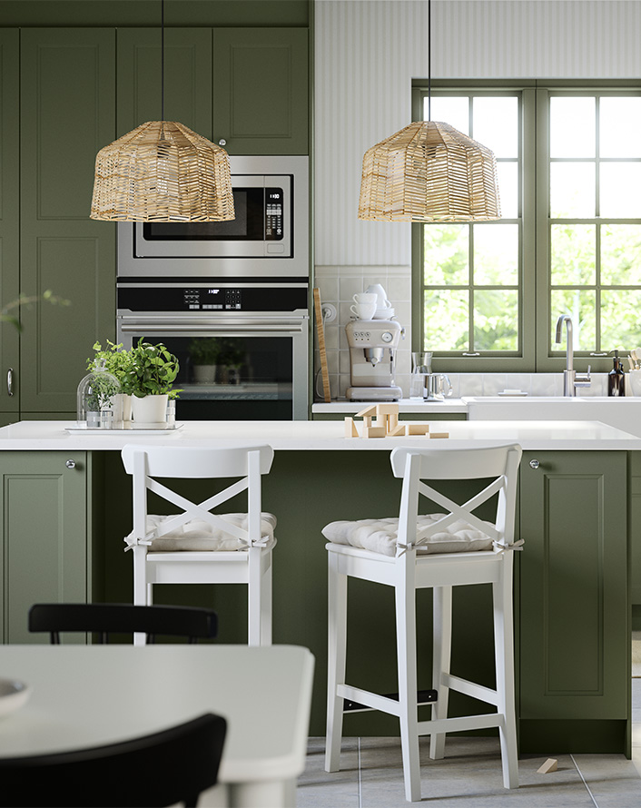 Green kitchen with island, white bar stools, and woven pendant lights.