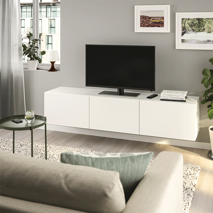Mueble de televisión blanco suspendido con televisor negro, mesa auxiliar verde oscuro, alfombra de pelo y decoración moderna.