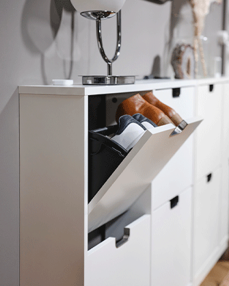 Mueble zapatero blanco con un compartimento abatible abierto, mostrando calzado guardado en su interior junto a una lámpara.