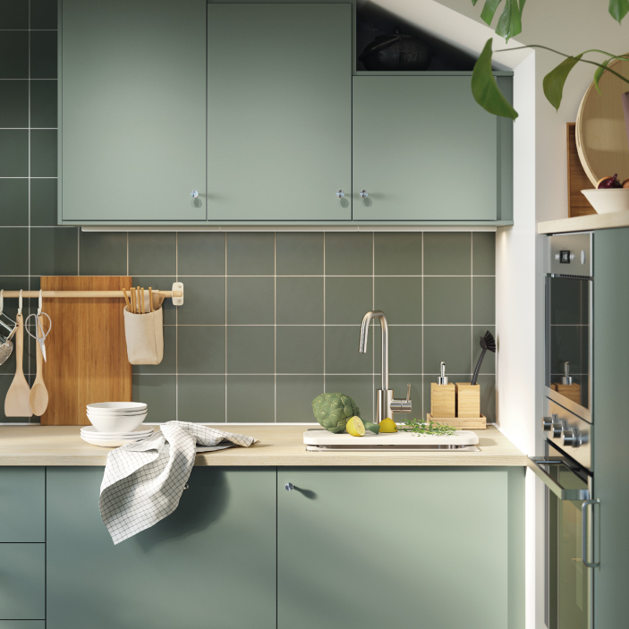 Cocina moderna con gabinetes y azulejos verde oliva, fregadero e encimera de madera.