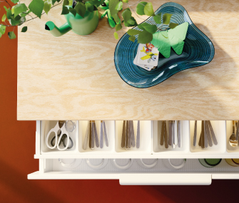 Vista superior de cajón de cocina abierto con cubiertos organizados bajo mesa de madera.