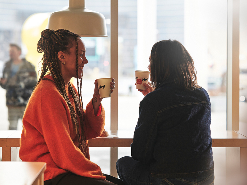 Two women chatting happily while drinking coffee by a window in a cafe.