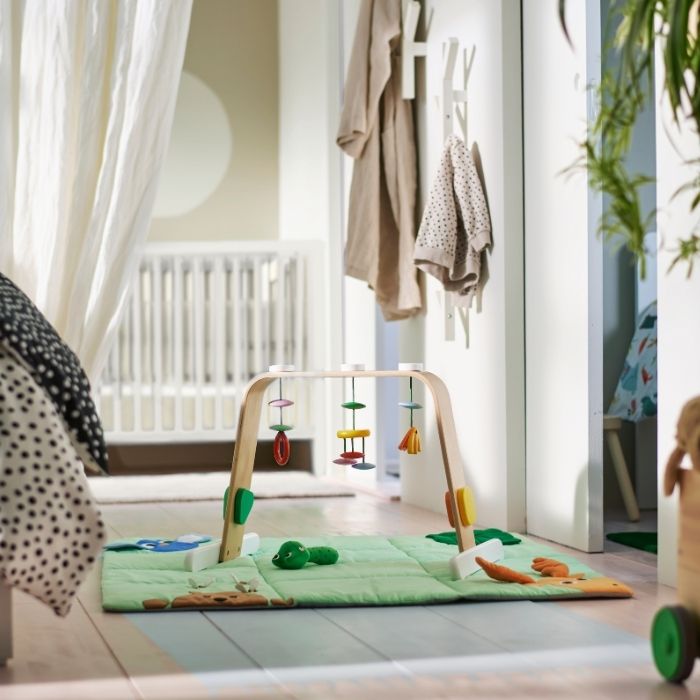 Un gimnasio para bebés LEKA sobre una alfombra verde en una habitación infantil blanca y beige.