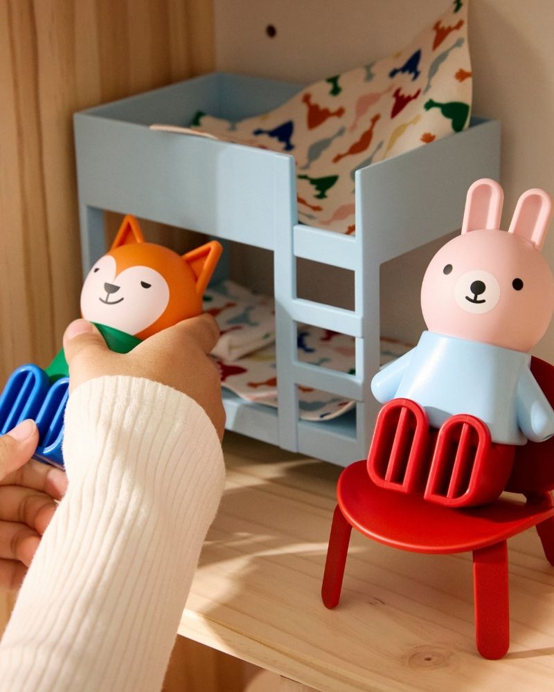 A pair of child's hands are playing with HUSET dolls and doll house.