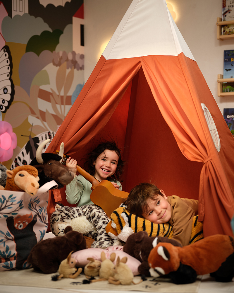 Two children in a HÖVLIG tent play with all the ALPTALL soft toys, including the Bengal tiger and red panda.