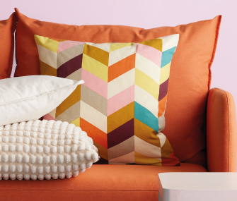 Cojines decorativos de colores sobre un sillón naranja, acompañados de un cojín blanco y uno texturizado.