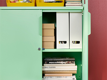 Mueble metálico verde menta con libros, revisteros y cajas organizadas en su interior.