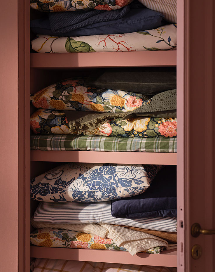 A pink wasdrobe with folded linens, including PJÄXE and ARENBOK duvet covers and pillowcases with different floral patterns.