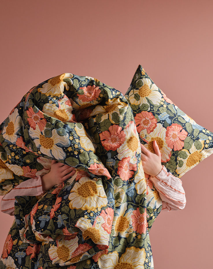 A person in a pink rooms is holding up an ARENBOK duvet cover and pillowcase so that they cover their face.