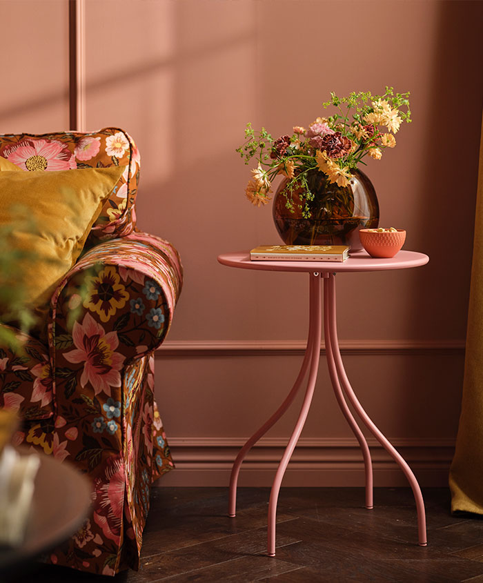 A TÅNEBRO side table in light pink stands in a pink living room next to an EKTORP sofa with a floral sofa cover.