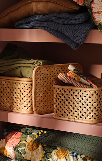 Beige VIELÅNGEN boxes in bamboo stand inside a pink wardrobe together with colourful bed linen.