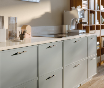 Mostrador de cocina con gabinetes gris claro, cafetera espresso y estantería de madera.