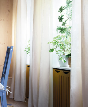 Cortinas translúcidas beige junto a una ventana con plantas de interior y silla azul.