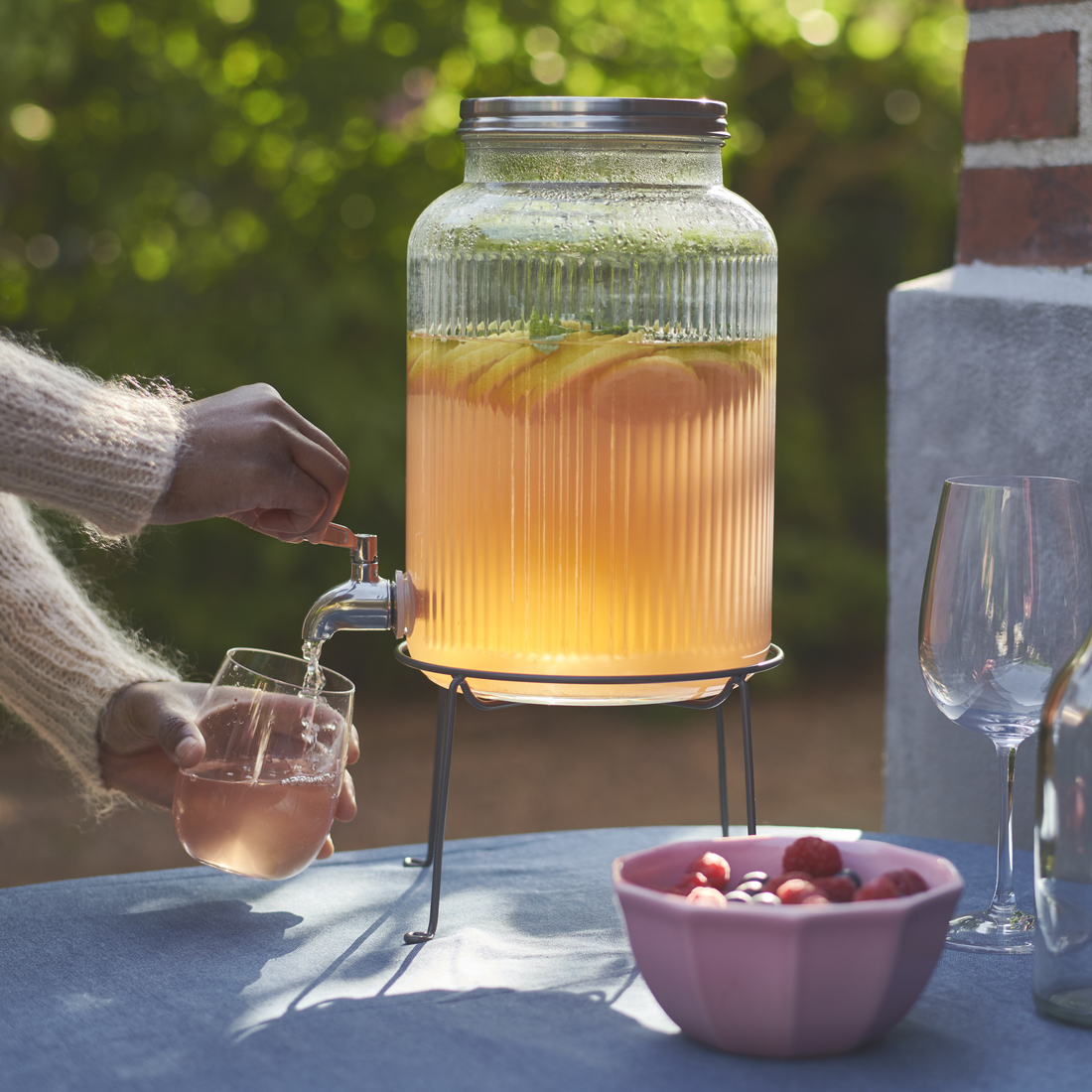 Una persona llena un vaso con limonada de un gran dispensador de vidrio.