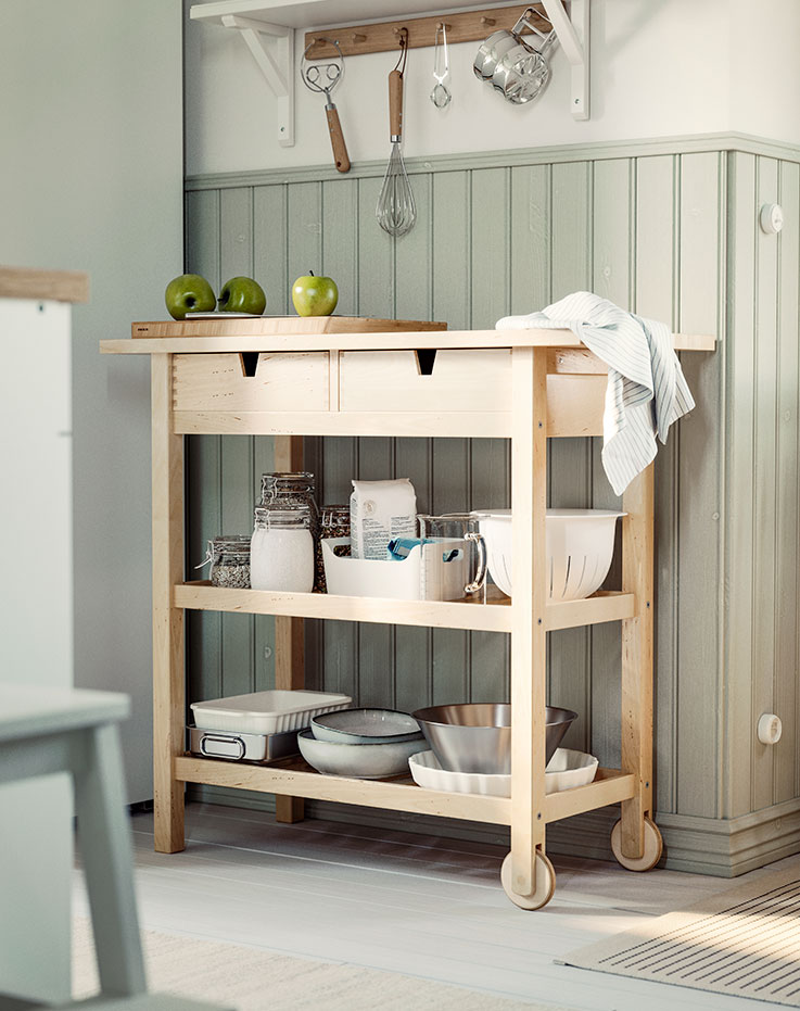 A fully loaded FÖRHÖJA birch kitchen trolley parked next to a sage green panelled wall in a kitchen.