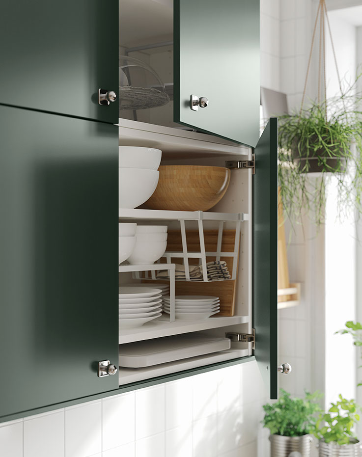 A kitchen cabinet with door ajar showing a PÅLYCKE clip-on basket, a VARIERA shelf insert and a BLANDA MATT bamboo bowl.