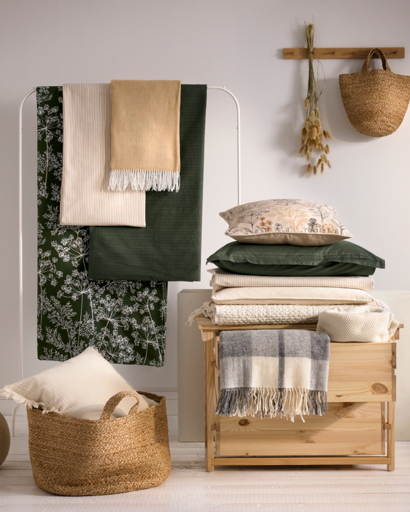 White clothing rail with hanging blankets, wooden storage unit with folded textiles and a basket.