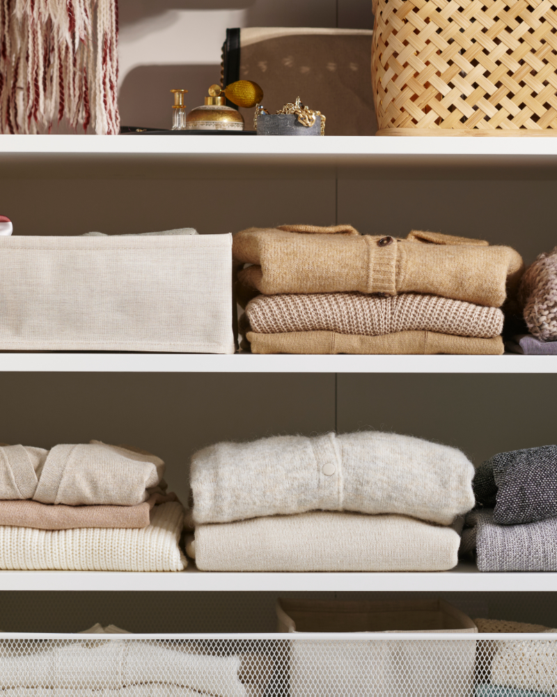 Neatly folded knit sweaters and fabric bins organized on closet shelves.