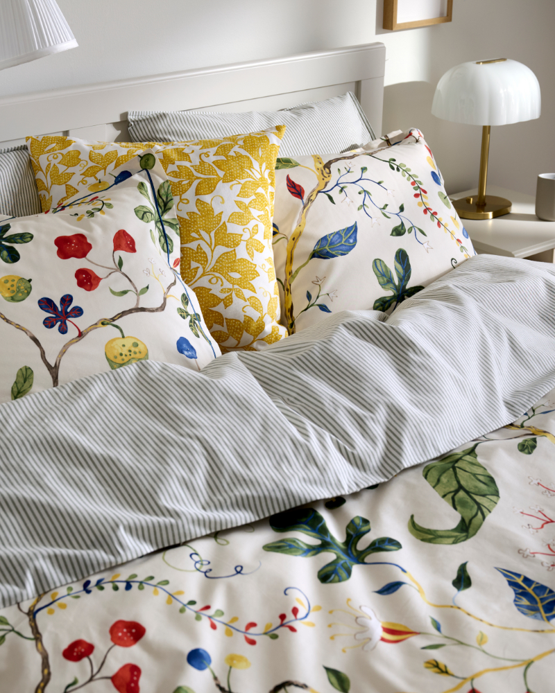 Bed with gray striped bedding and colorful floral pillows in white and yellow.