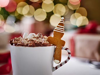 Taza de chocolate caliente con nata y galleta de jengibre en forma de árbol de Navidad, en un ambiente navideño.