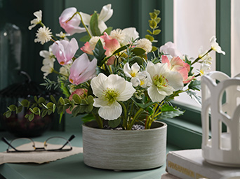 A FEJKA artificial flower arrangement in pink and white stands on a green windowsill next to books and a pair of glasses.