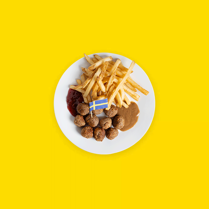 Plate with Swedish meatballs, french fries, jam, and gravy on a yellow background.   