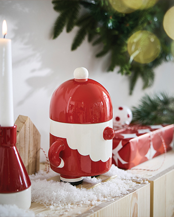 Santa Claus ceramic ornament on skis next to a candle and Christmas gift.