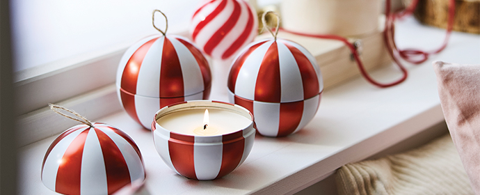Lit candle in a red and white striped container next to Christmas ornaments.