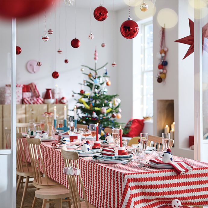 Christmas dining table set with striped tablecloth and hanging red baubles.